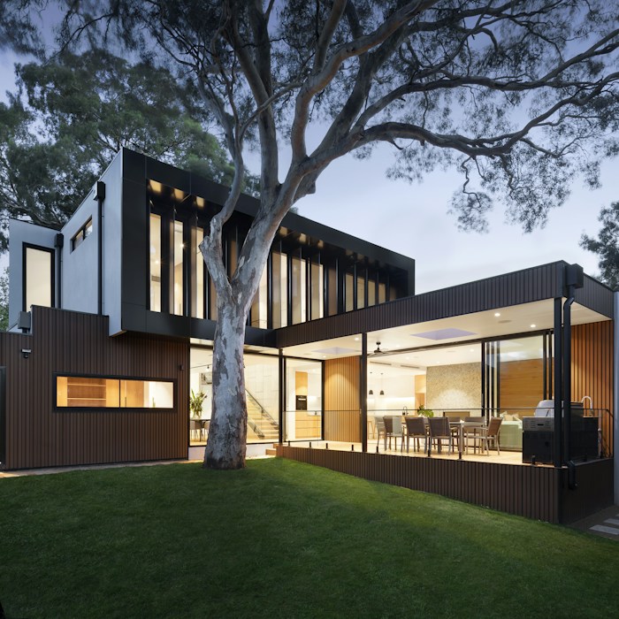 Contemporary single-storey residence at dusk with warm interior lighting visible through full-height glazing